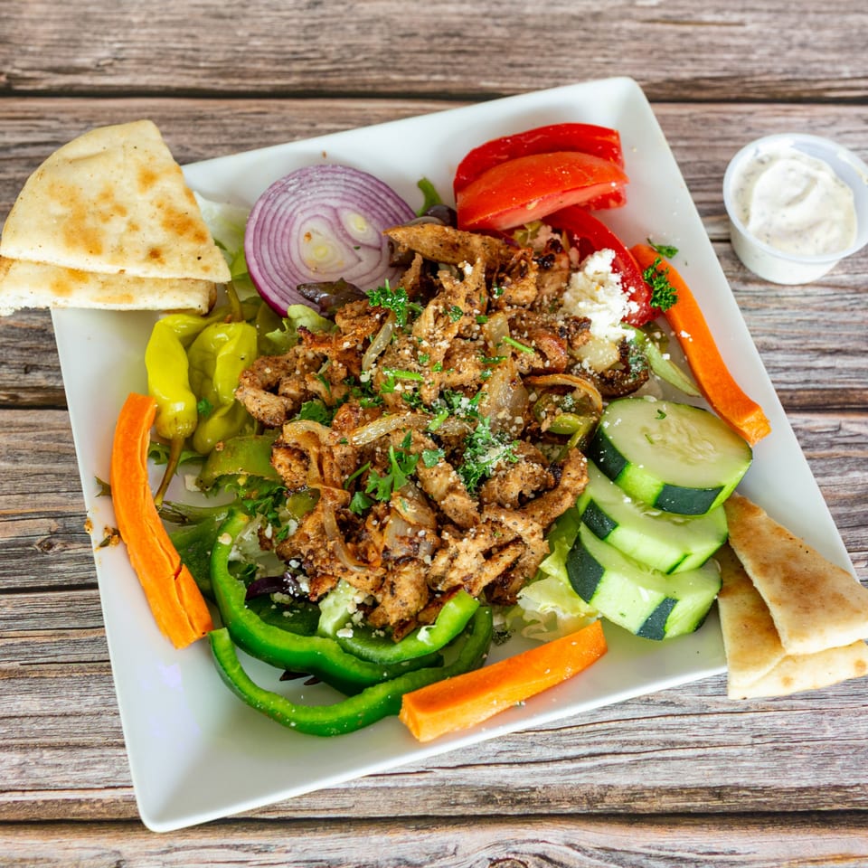 Greek Bites' chicken gyro salad with pita bread, vegetables, and a side of tzatziki sauce.