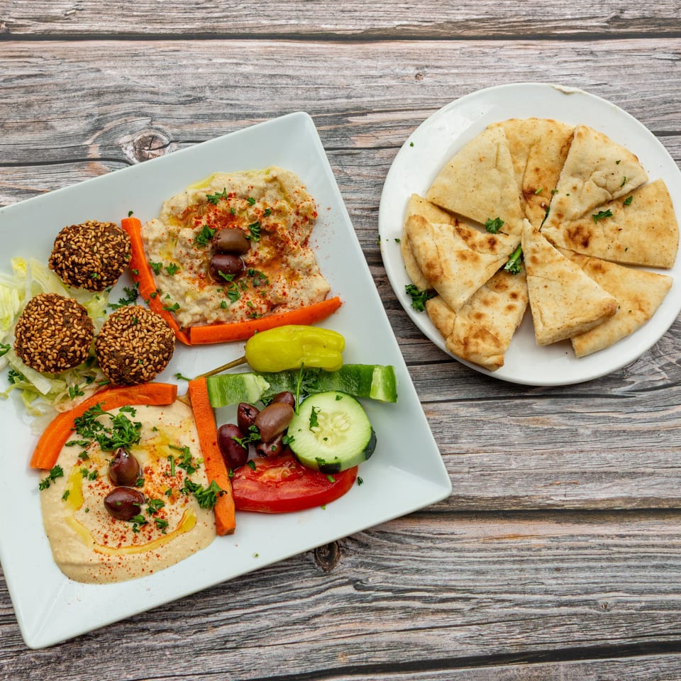 A platter of falafel, hummus, and fresh vegetables, with a side of pita bread on a wooden table.