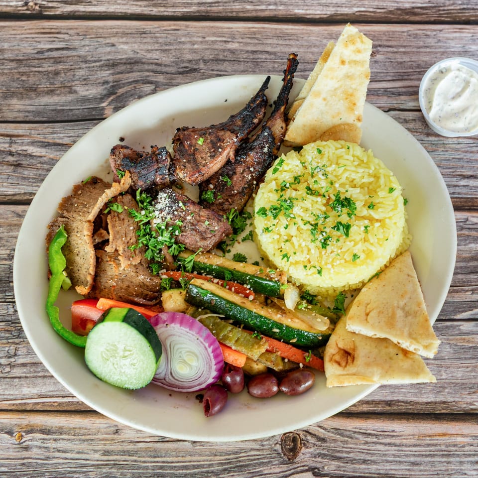 A Greek Bites platter with grilled lamb chops, gyro meat, rice, pita, vegetables, and olives.
