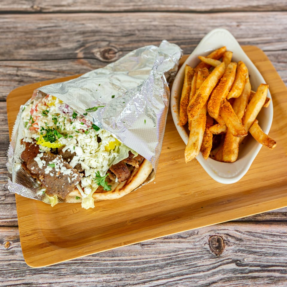 A Greek Bites gyro with meat, feta, and vegetables, wrapped in foil, next to a bowl of seasoned fries.