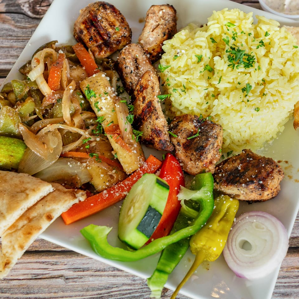 A Greek Bites platter with grilled chicken, yellow rice, sautéed vegetables, and pita bread.