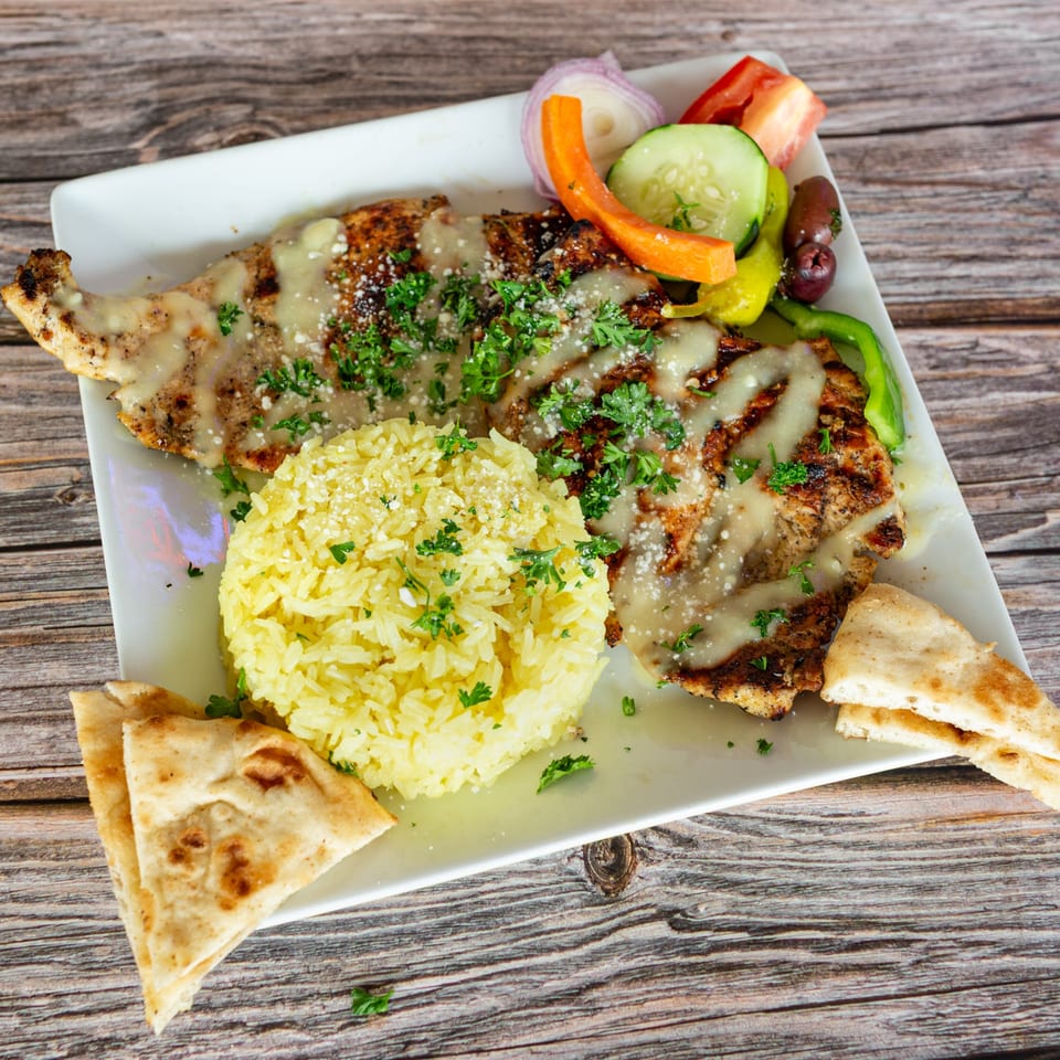 Grilled chicken with sauce, yellow rice, pita bread, and a side salad on a white plate.