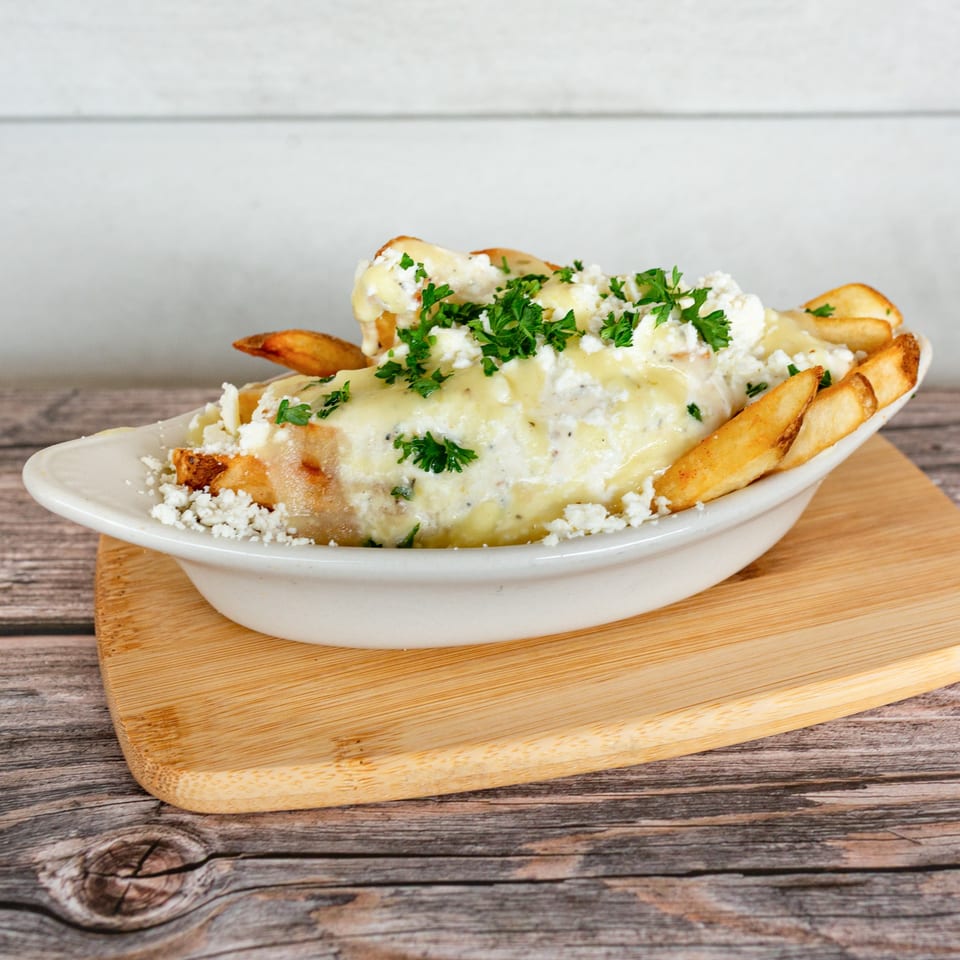 Greek Bites' fries topped with creamy sauce, crumbled feta cheese, and fresh parsley in a white dish.